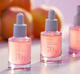 ANUA Peach 70 Niacin Serum bottle placed next to its box with peach extracts visible in the background.