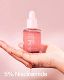 Clear pump bottle of the peach 70 niacin serum held up to natural light.