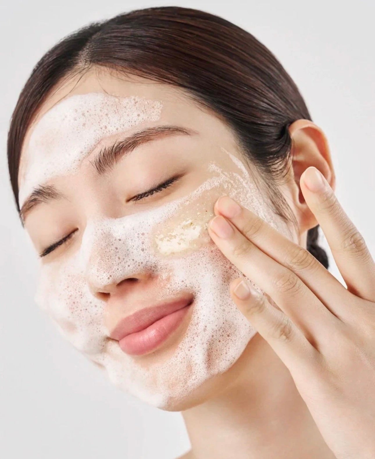 Woman with sensitive skin gently massaging Purito oat in gentle exfoliating face cleanser onto her damp cheeks.
